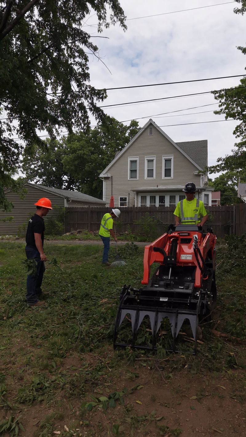 Three crew members in hard hats with the Kubota track loader on a lot being cleared, a house behind