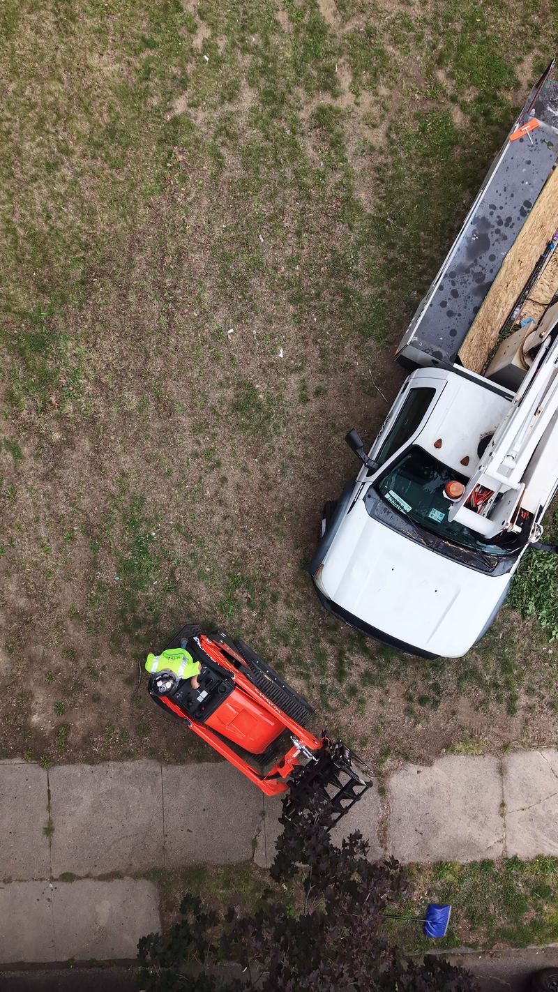 Overhead drone view of the bucket truck and the orange track loader working at the edge of a lot