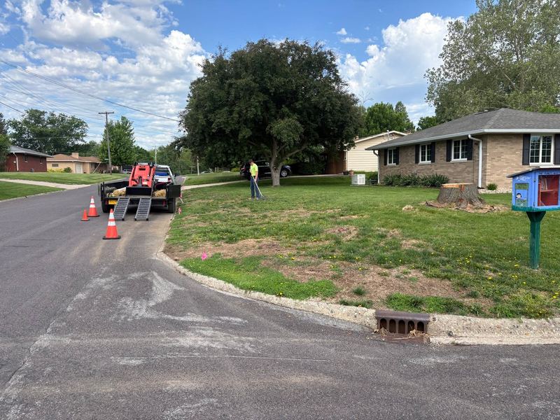 Bare, rough strip of yard along the curb before grading, a track loader on a trailer at the street