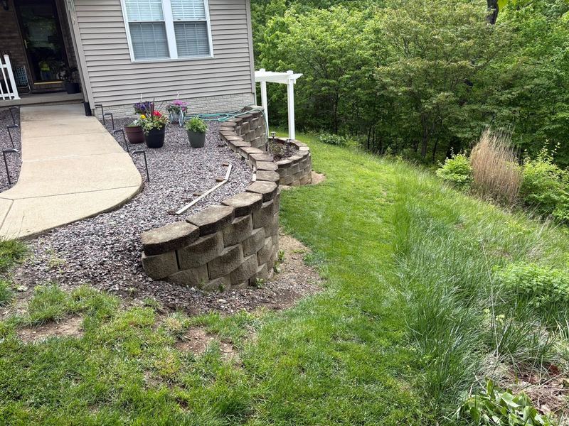 Curved tan block retaining wall with a gravel bed beside a front walk