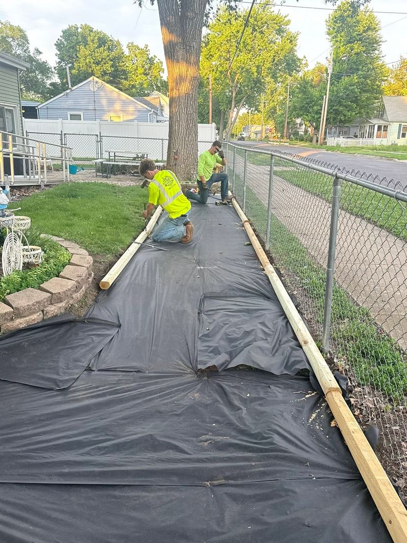 Black weed fabric and wood edging laid along a fence where the walkway will go