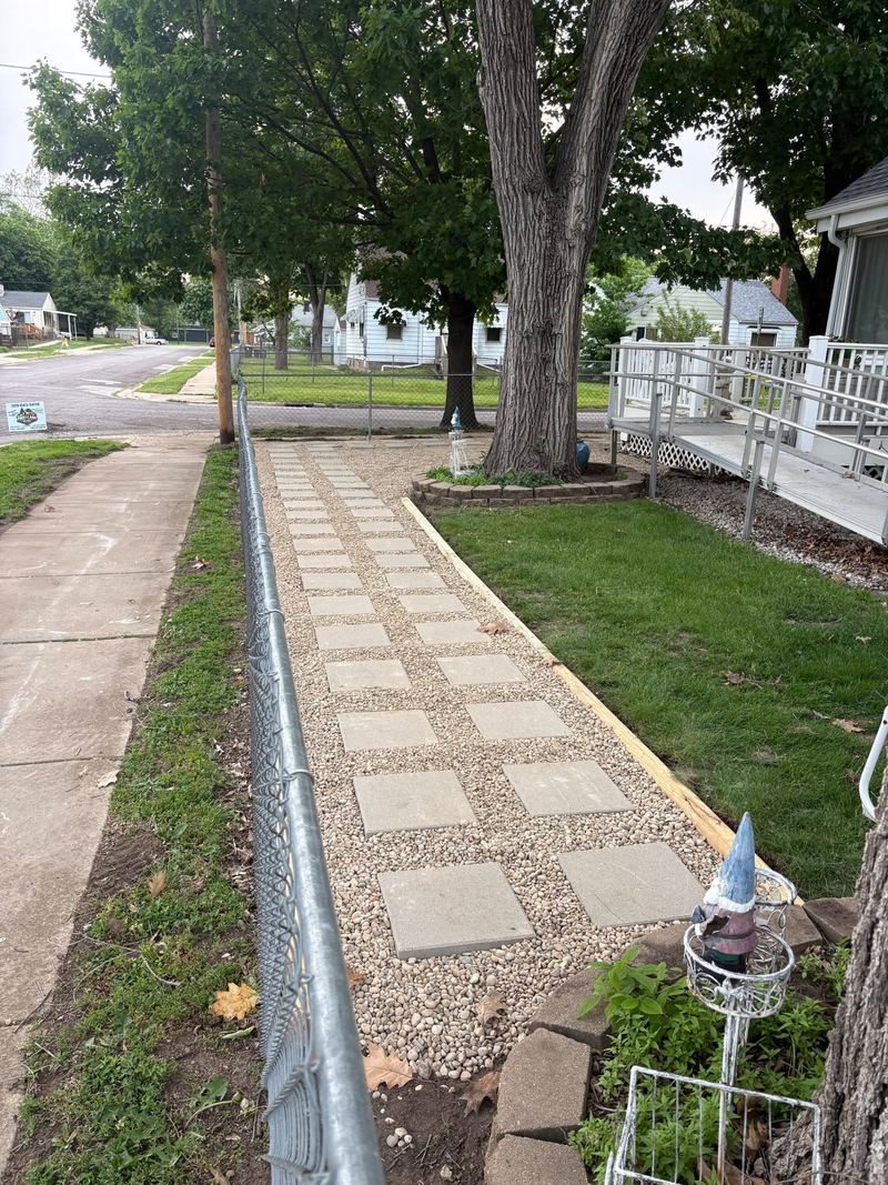 Walkway of square stepping stones set in gravel with wood edging, along a fence